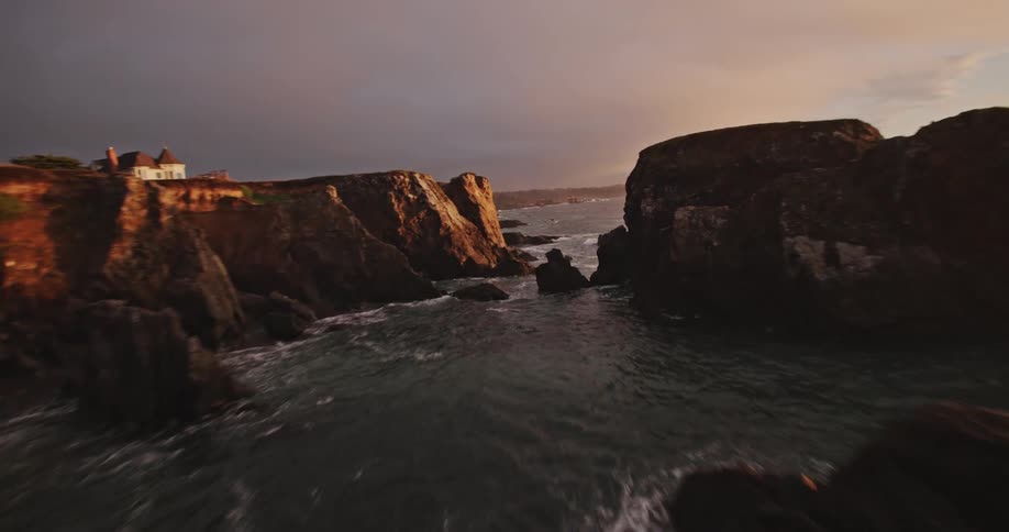Aerial view of the sea crashing against the rocky coastline at dawn
