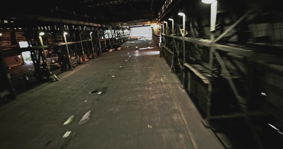 A motorcycle is speeding through an industrial area with large metal structures and containers