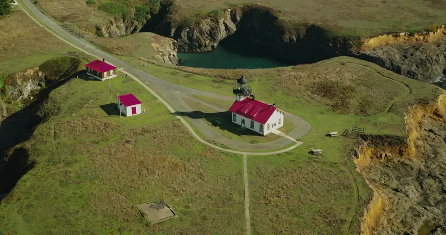 Charming redroofed lighthouse stands atop rugged cliffs watching over the vast blue ocean