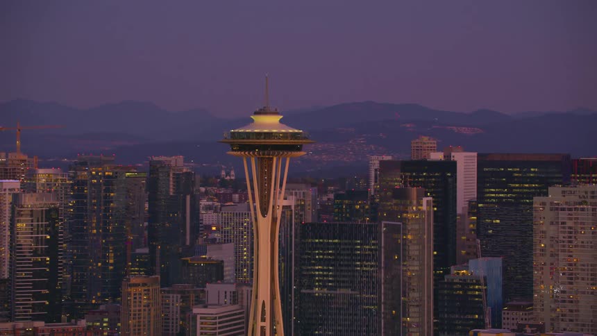 Ionic space needle stands illuminated against the twilight sky surrounded by seattles vibrant skyscrapers