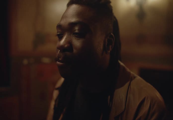 A person with dreadlocks is sitting in a dimly lit room with a warm rustic ambiance eating