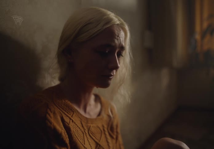 Sad blonde woman sits on the floor and leans against a wall