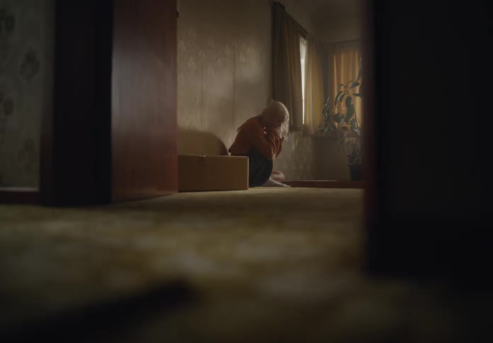 Downcast blonde woman crouches on the floor near the wall