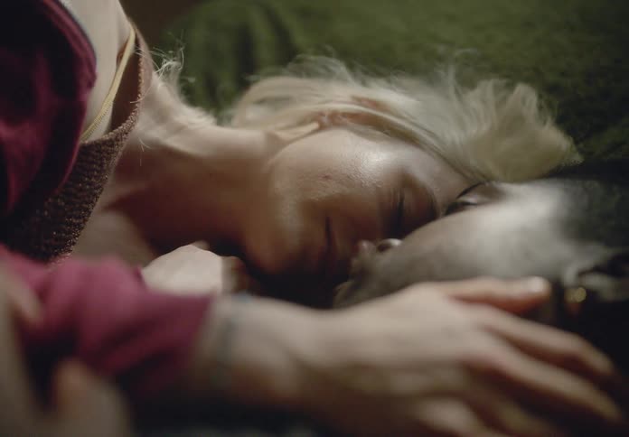 A couple is lying on a green bed in a dimly lit room with a window cuddling playfully