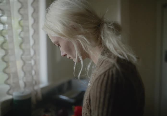 Blonde woman with a brown sweater slices up tomatoes in the kitchen