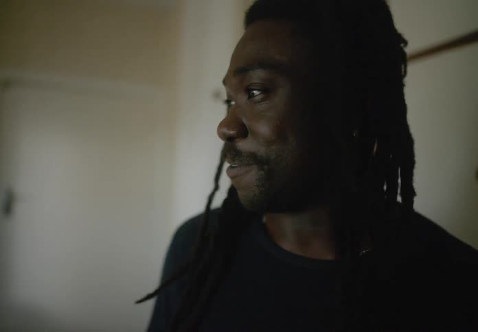 Man smiles while standing indoors and talking to another