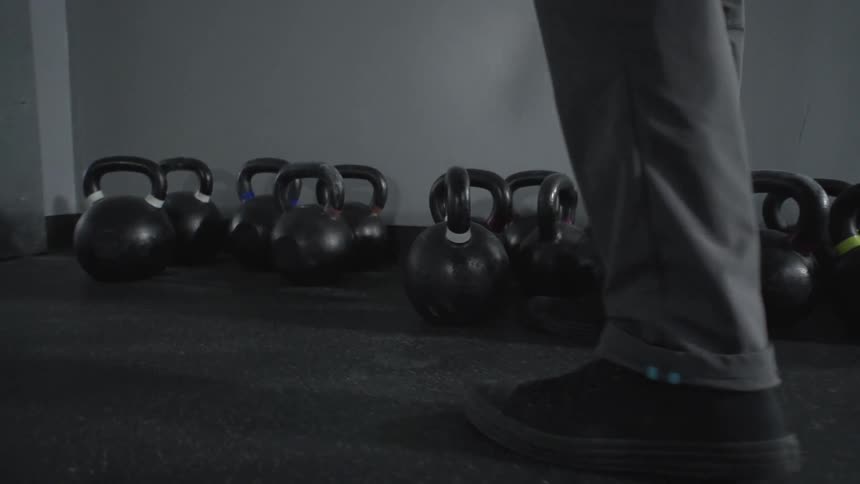 Kettlebells line the floor of a gym and man picks one up.