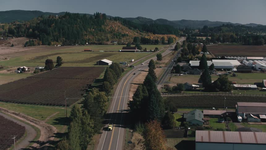 Aerial view of a highway passing through farms and mountains with forests in the background