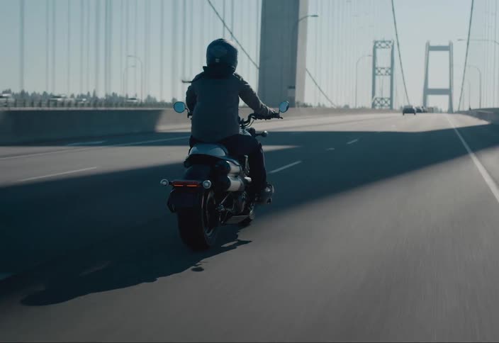 Motorcyclist rides a motorcycle across a bridge near a forest on a sunny day