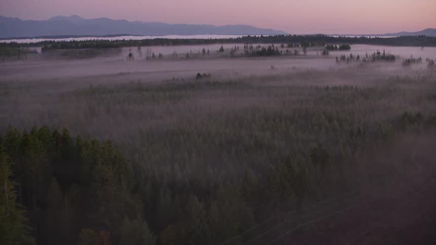 Dense fog covers the mountains and the forests and the lake that separates them under a red sky