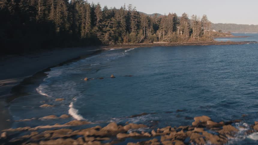 Landscape of a calm sea reaching the wooded coast with mountains in the background