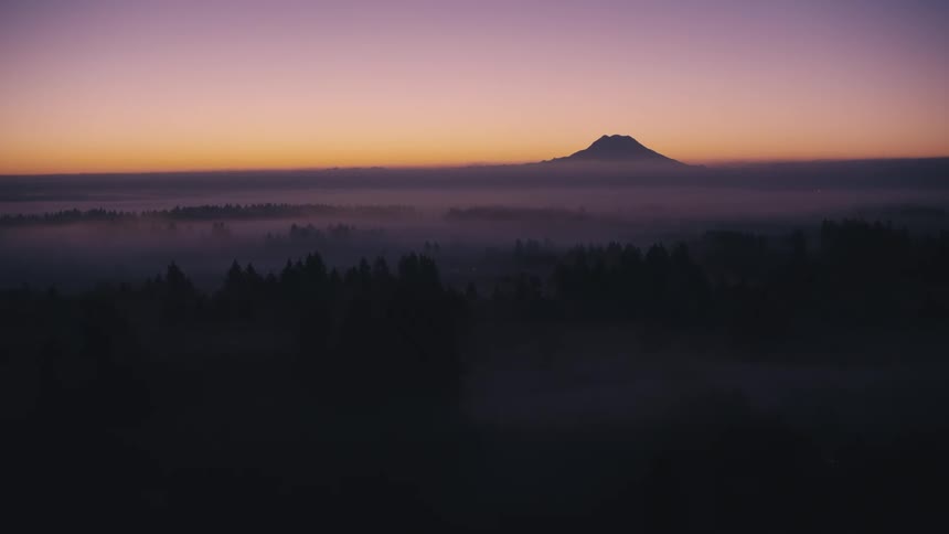 Mountain standing silhouetted against a red tinted horizon towers over fog covered forested terrain