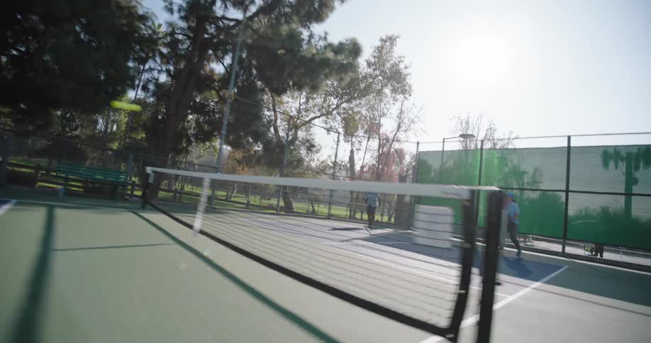 Two couples playing pickleball on an outdoor court surrounded by tall trees and a fence
