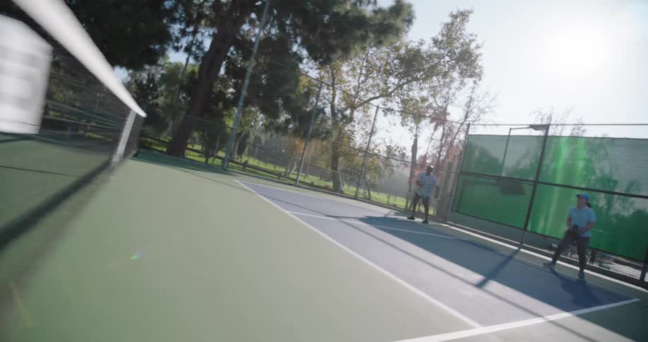 Two couples playing pickleball on an outdoor court surrounded by tall trees and a fence