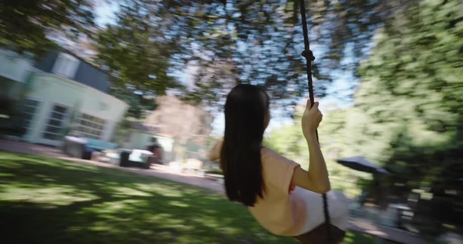 A little girl is swinging on a tree swing in the backyard behind a house