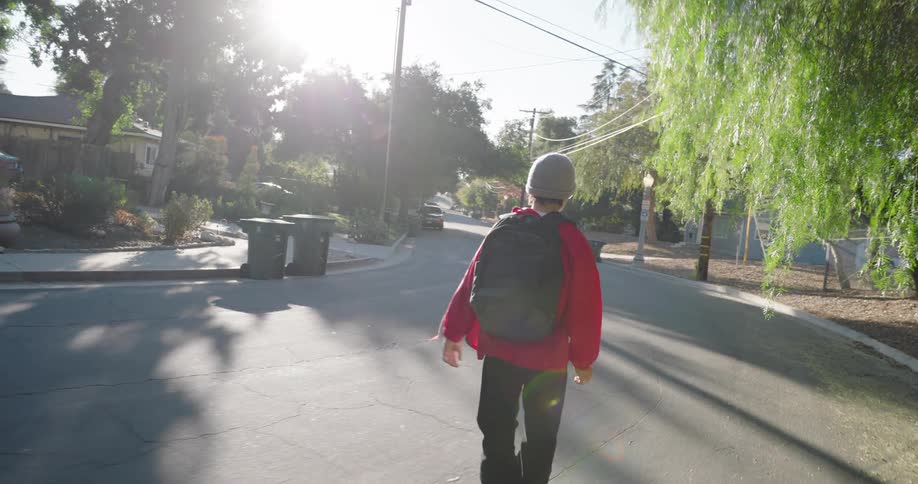 A teenager wearing a red jacket and black pants skateboards on a residential street