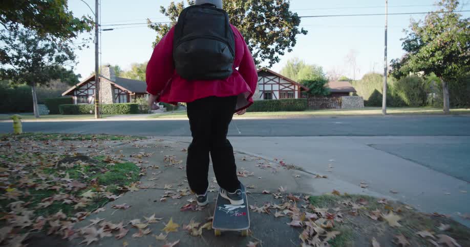 Boy with a backpack skateboarding down the sidewalk and doing a trick