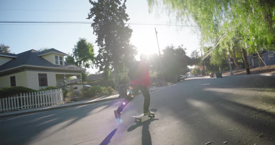 A teenage boy skateboards on a residential street on a sunny day