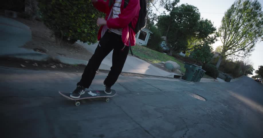 A teenager wearing a red jacket and black pants skateboards on a residential street