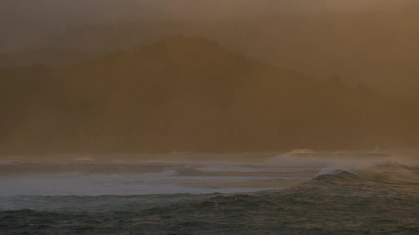 Landscape of waves in an ocean with the silhouette of mountains in the background