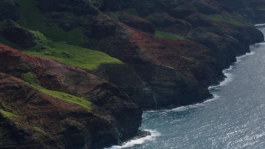 The camera is panning up the coastline where the black cliffs with the patches of green grass meet the water
