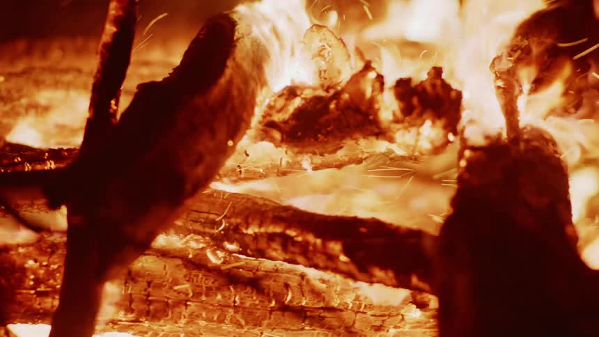 Flames engulf roughhewn logs highlighting the texture of the wood and the intense heat of the fire