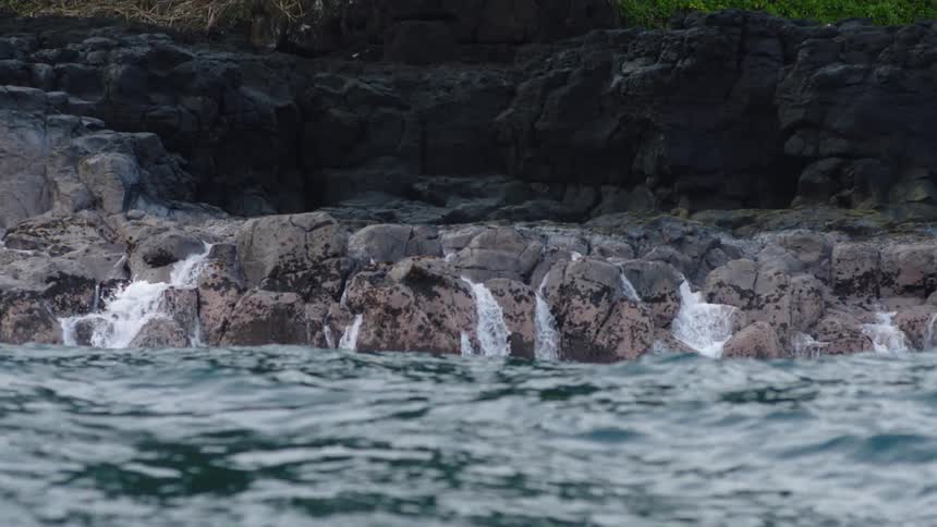 Water cascades over a rocky outcrop into a turbulent sea creating a frothy white spray against the dark textured rocks