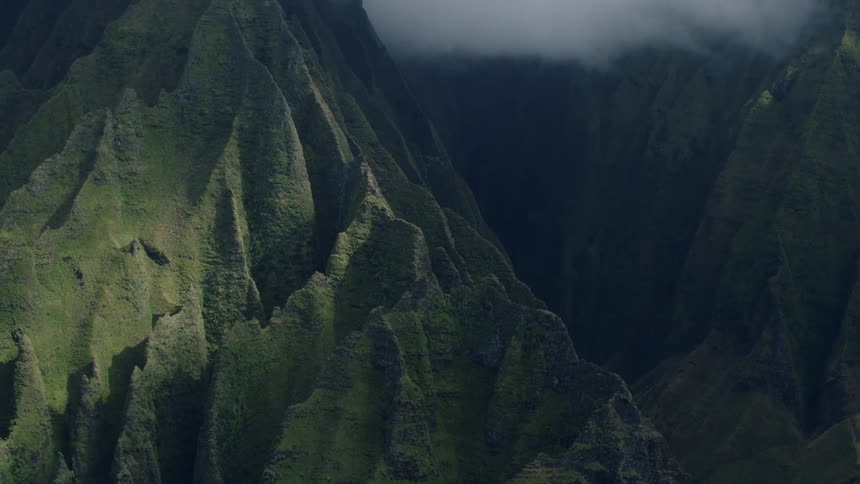 A lush steep mountain range with rugged terrain and dense vegetation is partially shrouded in mist