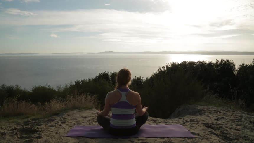 Woman meditating on a mat on the beach