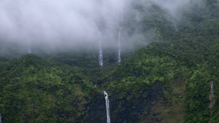 Fog hovering over small waterfalls on a lush cliffside in a tropical island