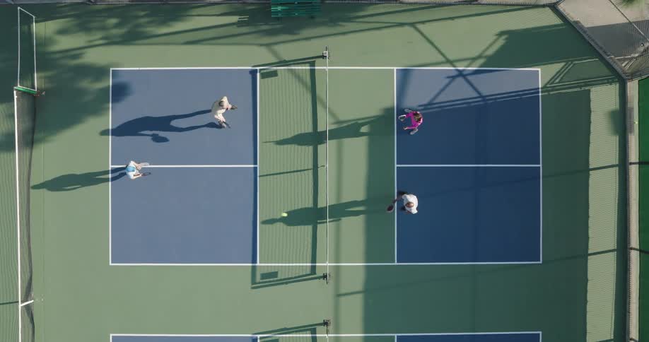 An aerial view of a doubles pickleball game in progress with two players on each side of the net casting long shadows on the court