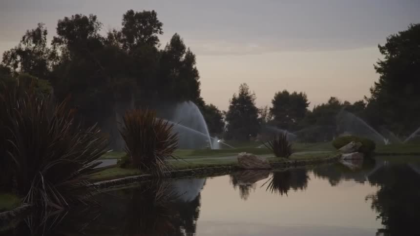 Sprinklers watering a lawn next to a body of water on a cloudy day