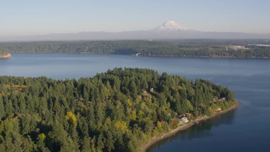 A densely forested peninsula juts into a calm lake with a sliver of land visible in the distance under a hazy sky