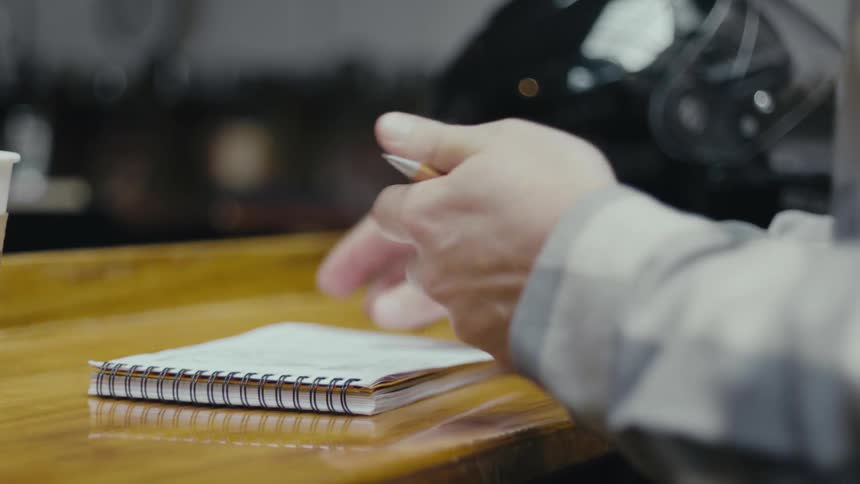 Man sitting at a table next to a motorcycle helmet prepares to write in a notebook