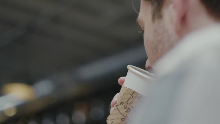 Man sitting in a cafe takes a sip from a disposable cup