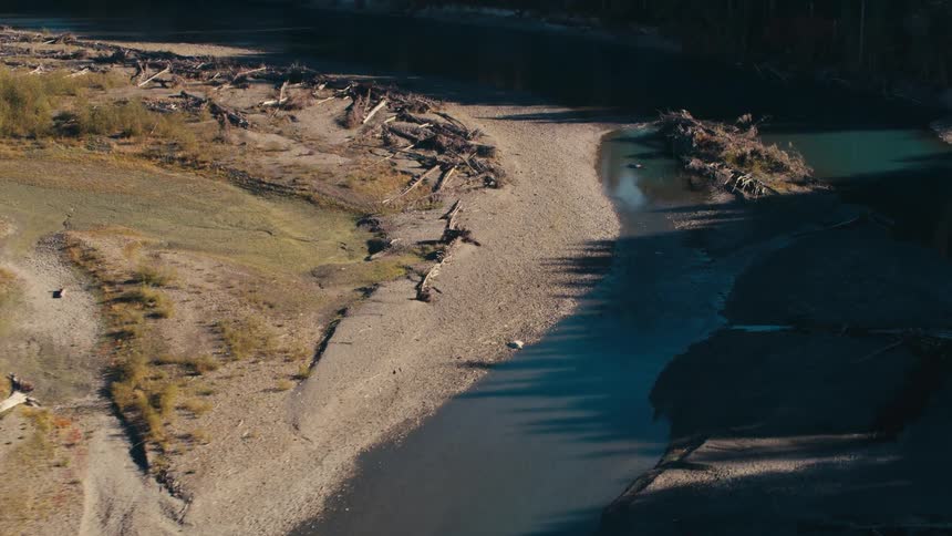 An aerial view shows a winding river course through a barren landscape revealing exposed earth and scattered debris alongside patches of remaining forest