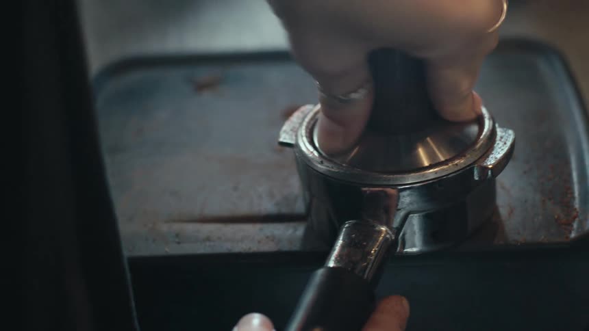 A hand is pressing down on a coffee tamper to compact coffee grounds in a portafilter