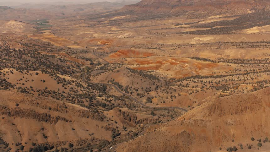 A winding road that cuts through a brown hilly desert landscape with distant mountains