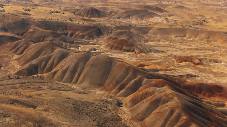 An aerial shot reveals a rugged dry landscape with a network of brown hills and valleys