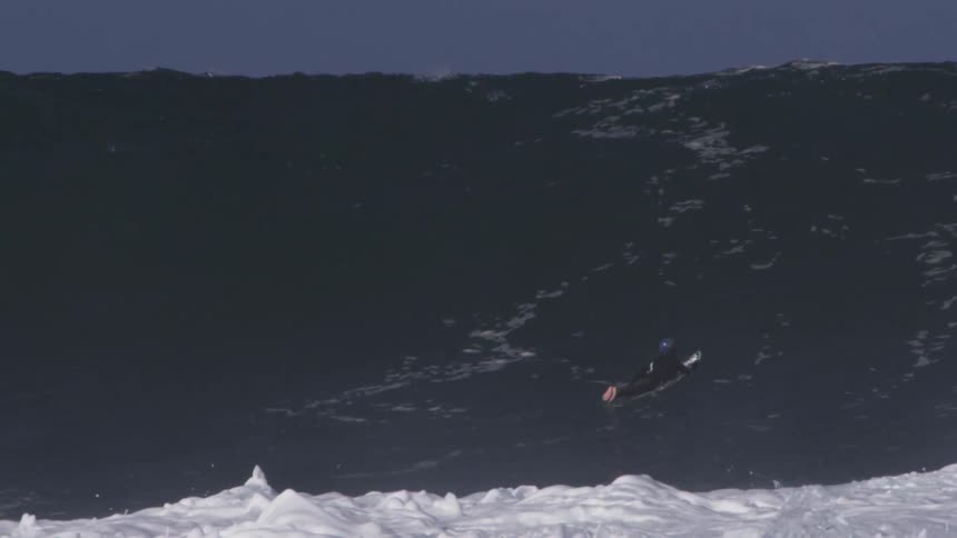 A surfer floating as a large wave flows under him