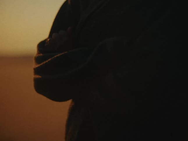 The crossed arms of a person wearing a longsleeved coat at sunset or sunrise
