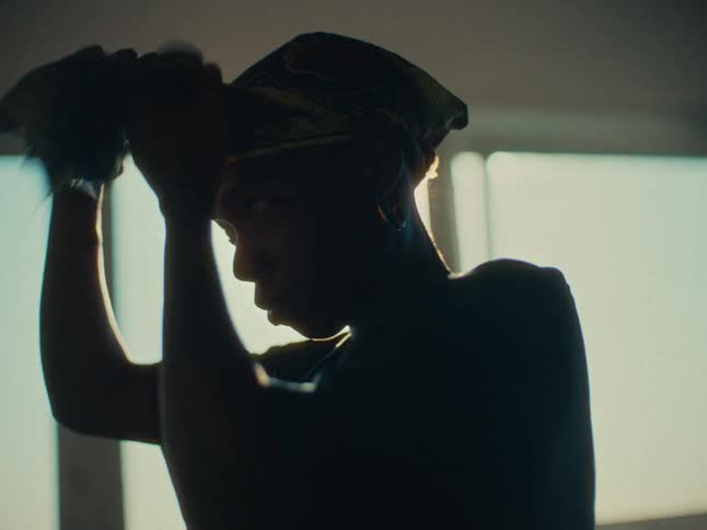A woman silhouetted tying a headscarf around their head
