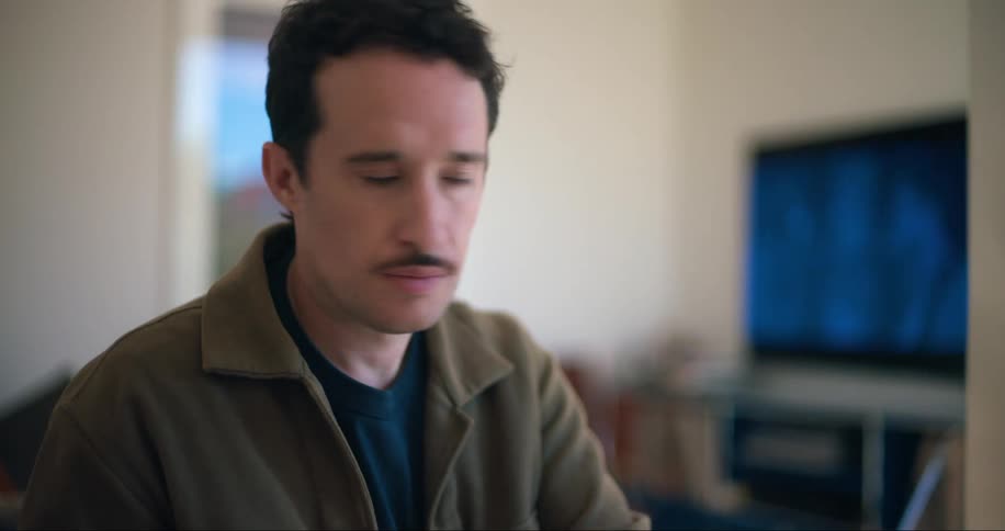 A man flips through a magazine then types on his laptop