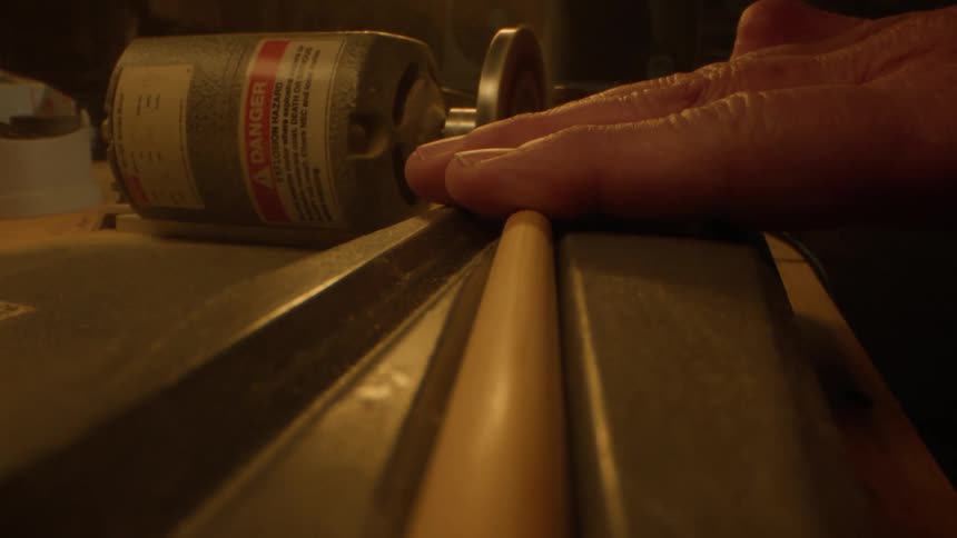 Person feeds a wooden rod through a sander casting sawdust to the side