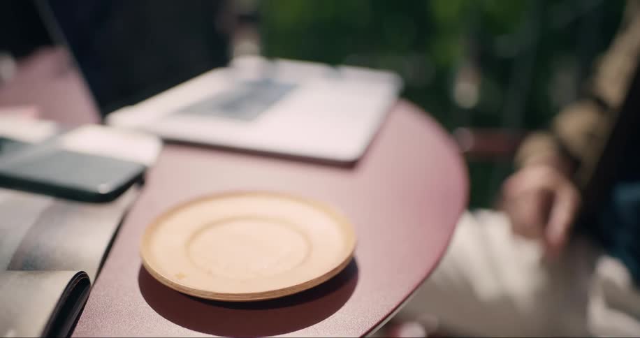 A man drinking from a small ambercolored glass cup on a saucer with a smartphone a notebook and a pen visible on the table in the background