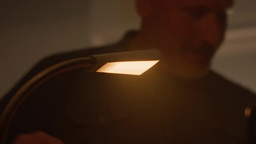 Closeup of a man lighting a small table lamp in a dimly lit room