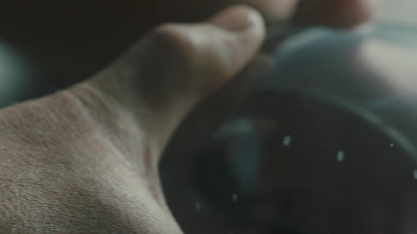 Closeup of hands holding a glass ball reflecting dim light moving it over a surface