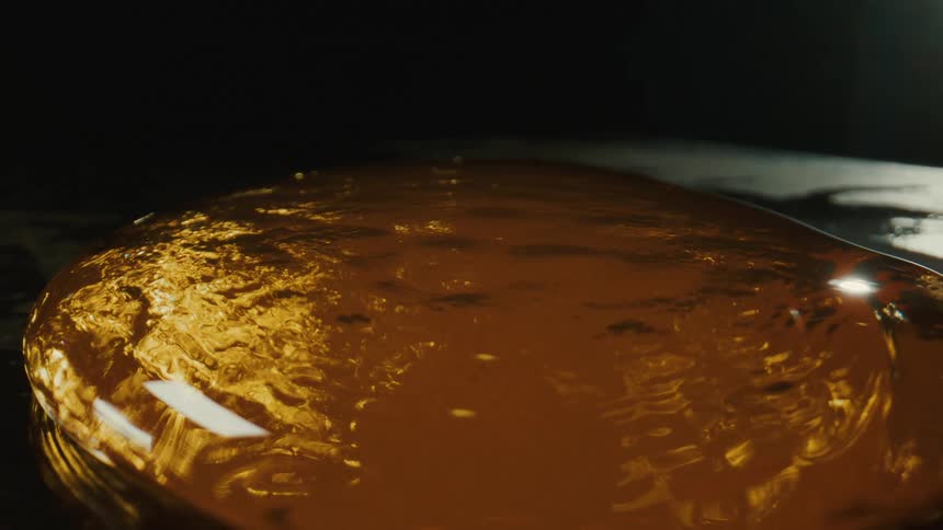 A closeup of a glossy ambercolored blob reflects light against a dark background