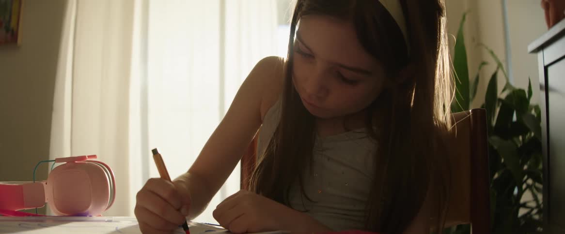 Young girl sitting at her desk in her room drawing with markers in a book