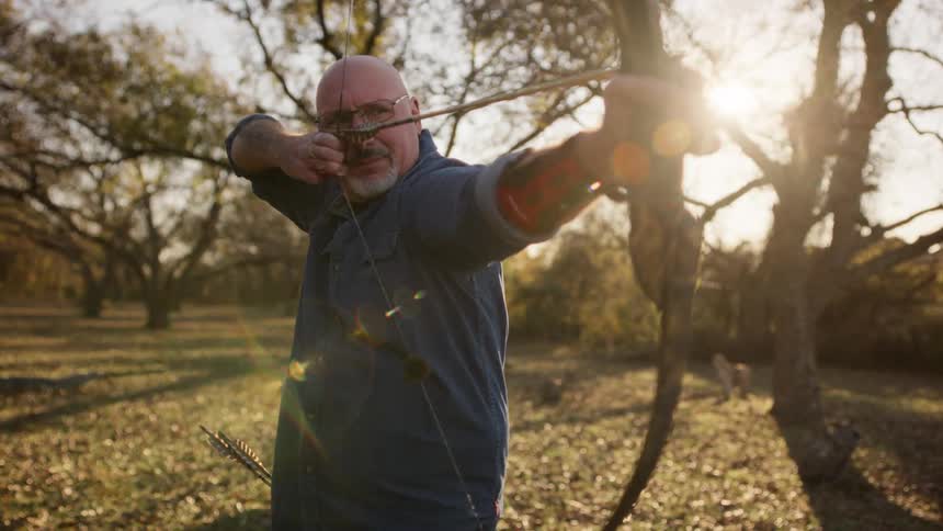 A man is aiming a bow and arrow on a sunny day